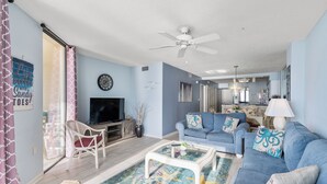 A living room with a blue sofa, a white armchair, a glass coffee table, and a television.