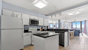 A modern kitchen with white cabinetry, a central island, and a dining area with a view.