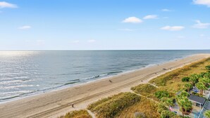 A beach with a path leading to a building with a flag, overlooking the ocean.