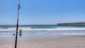 A beach with a fishing rod and a pier in the background.