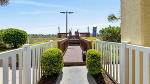 A wooden pathway leading to a building with white railings and a clear sky.