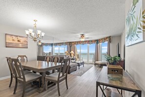 A spacious living room with a dining area, large windows, and a view of the ocean.