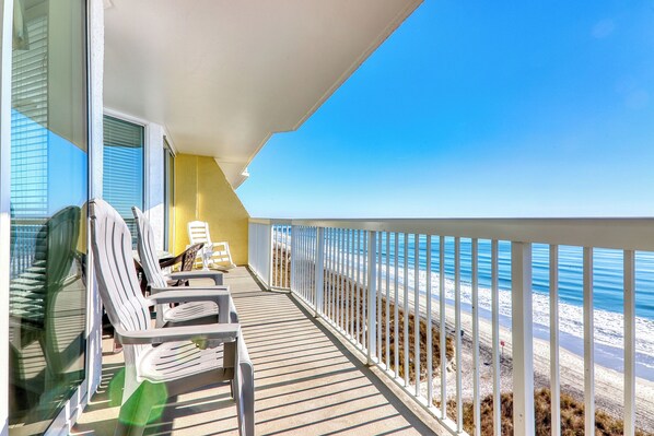 A balcony with white chairs, a yellow wall, and a view of the beach.