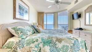 A bedroom with a bed, a ceiling fan, a television, a dresser, and a window with curtains.