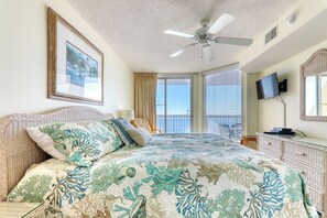 Un dormitorio con cama, ventilador de techo, televisor, cómoda y ventana con cortinas.