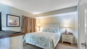 A bedroom with a bed, bedside table, lamp, and a framed picture on the wall.