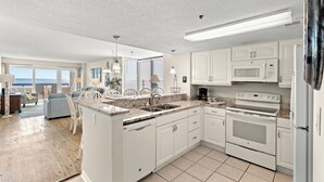 A modern kitchen with white cabinets, a built-in oven, and a microwave. There is a large window providing a view of the outdoors. - Sea Pointe 908 -Oceanfront 3BR/2BA Condo (North Myrtle Beach)