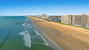 A beach with a pier extending into the ocean, adjacent to a row of multi-story buildings with balconies. - Sea Pointe 908 -Oceanfront 3BR/2BA Condo (North Myrtle Beach)
