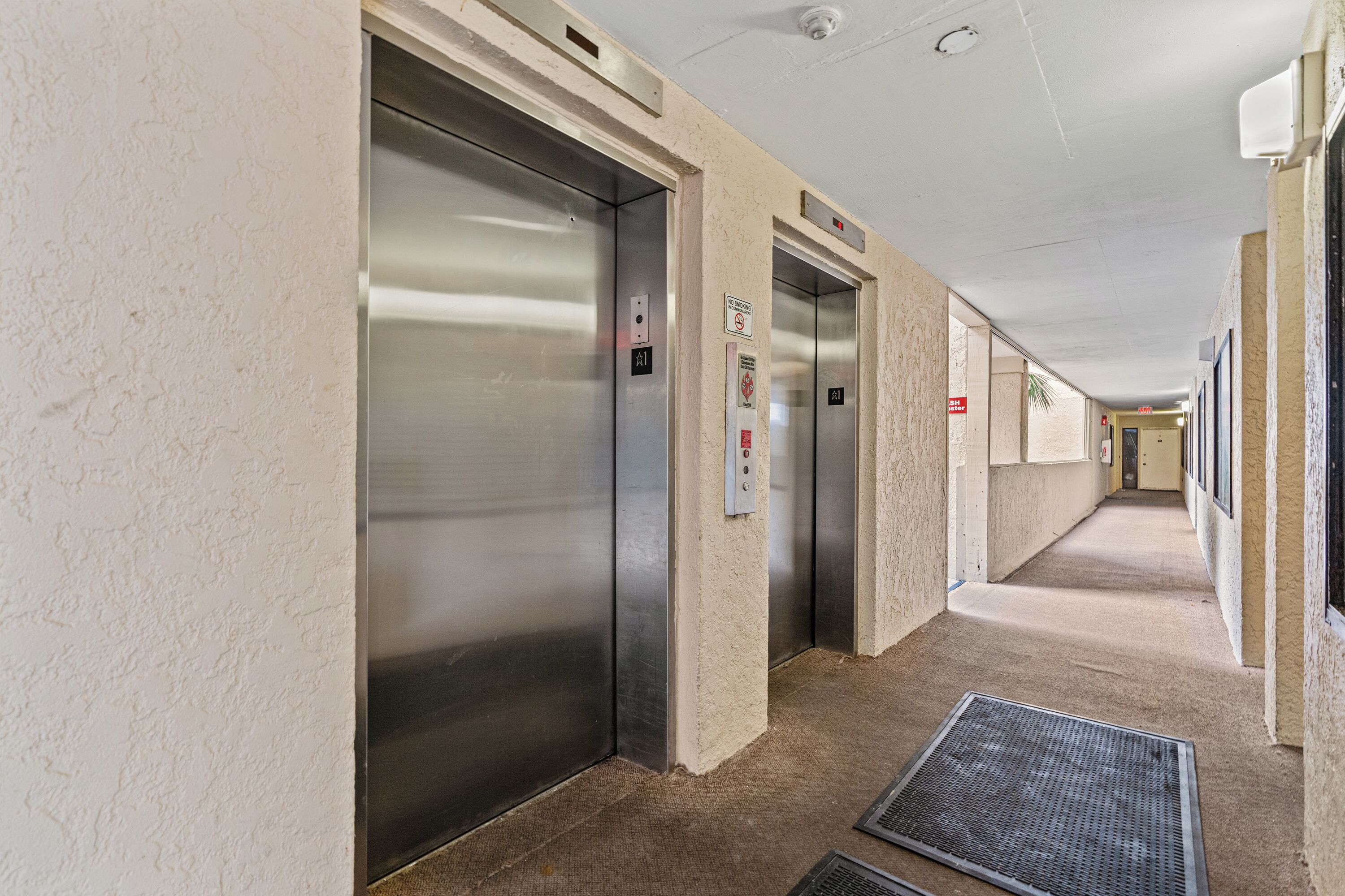 A hallway with two elevators and a carpeted floor.