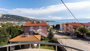 A coastal residential area with terraced houses, a clear view of the sea, and a distant mountain range. - Holiday apartment by the sea with barbecue and panoramic view (Baška)