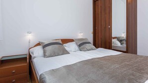 A bedroom with a wooden bed, two bedside tables, a wardrobe, and a mirror. - Holiday apartment by the sea with barbecue and panoramic view (Baška)