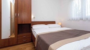 Un dormitorio con un armario de madera, una cama con colcha marrón y una ventana con cortinas de encaje.