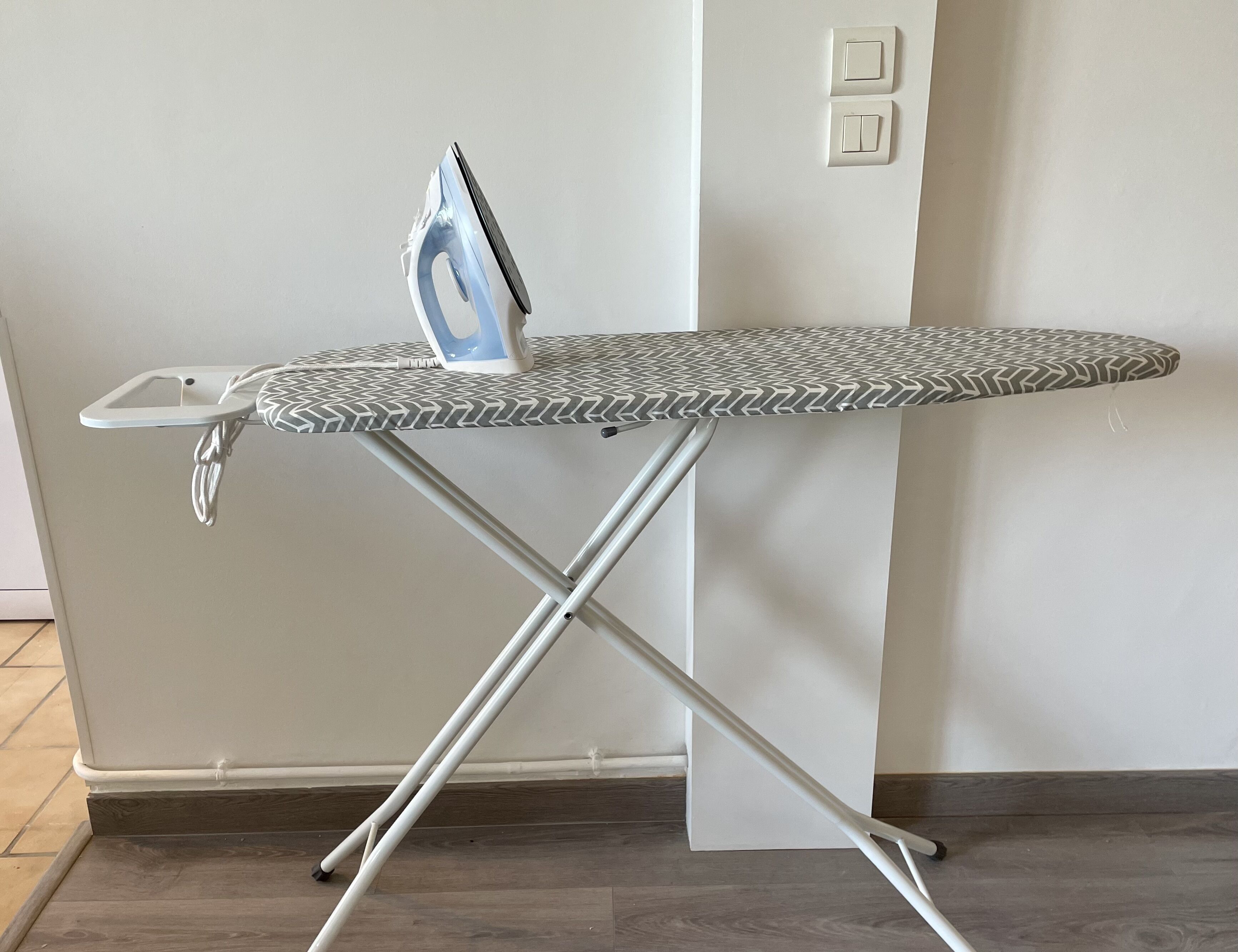 Une planche à repasser avec une housse à motifs, un fer à repasser intégré et un câble d’alimentation.