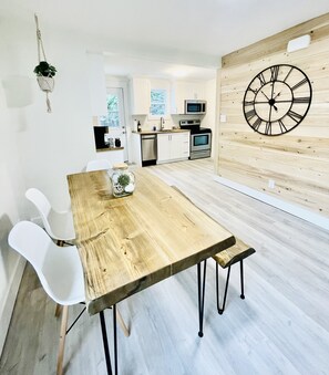 Una cocina moderna con armarios blancos, una mesa de comedor de madera con patas negras y un gran reloj de pared.