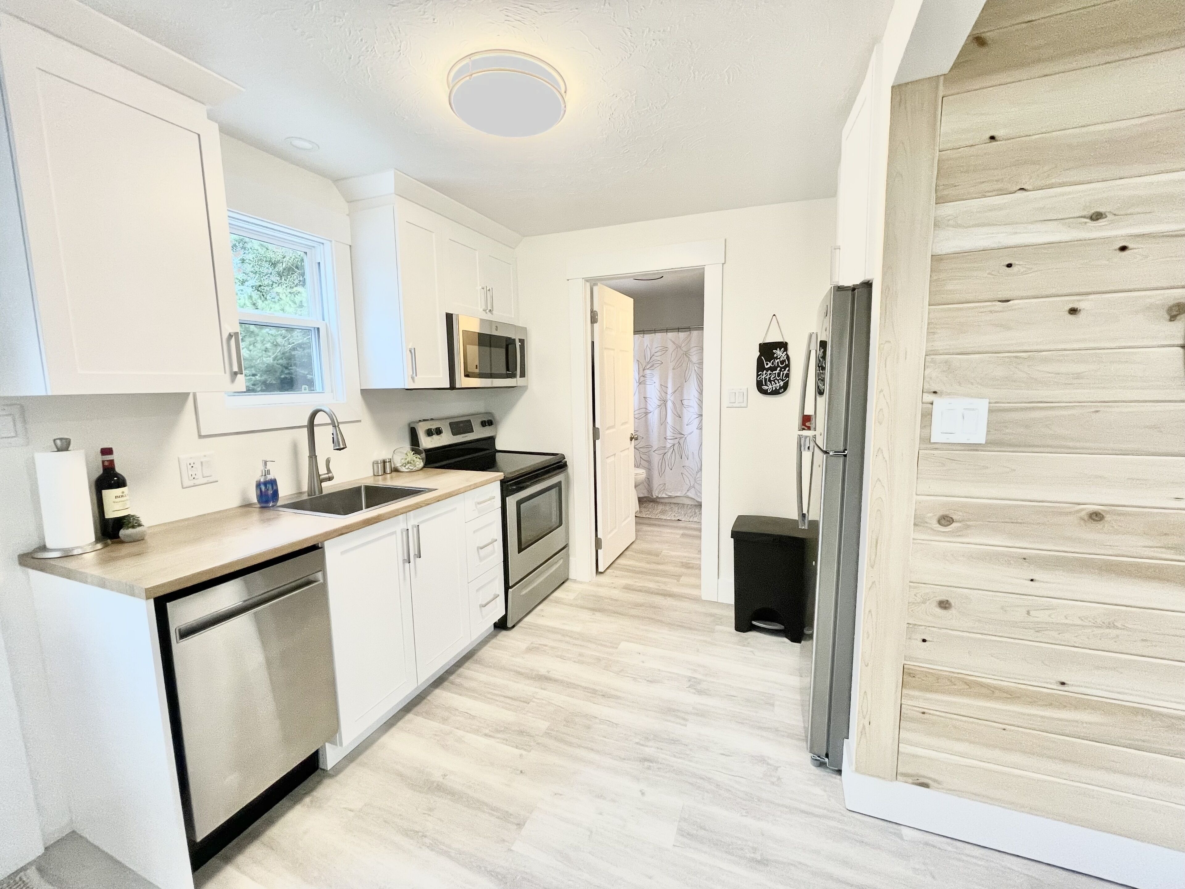 A modern kitchen with white cabinets, stainless steel appliances, and a wooden floor.