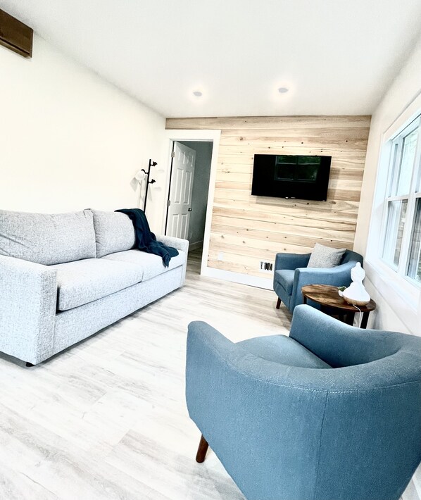 Una sala moderna con un sofá gris, un sillón azul y una pared de madera con un televisor de pantalla plana.