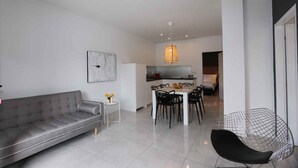 A modern living room with a grey sofa, a dining table with chairs, a black wire chair, and a kitchen in the background. - Holiday apartment with air conditioning and only 220 meters from the beach (Šilo)