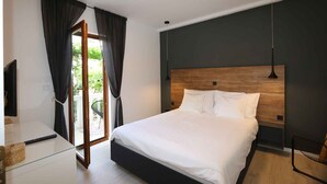 A modern bedroom with a large bed, a wooden headboard, a glass bedside table, and a view of the outdoors through a sliding door. - Holiday apartment with air conditioning and only 220 meters from the beach (Šilo)