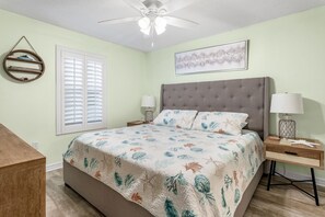 A bedroom with a bed, two bedside tables, a ceiling fan, a window with blinds, and a wall-mounted shelf. - 19th Floor Pelican Beachfront with Ocean View (Destin)