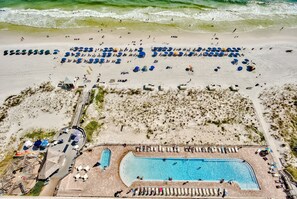 An aerial view of a beach resort with a swimming pool, beach umbrellas, and lounge chairs. - 19th Floor Pelican Beachfront with Ocean View (Destin)