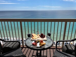 A balcony with a table set for a meal, overlooking a beach and the ocean. - 19th Floor Pelican Beachfront with Ocean View (Destin)