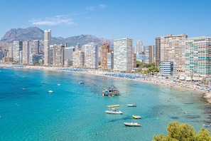 Un paysage urbain côtier avec de hauts immeubles, une plage et des bateaux sur l’eau.