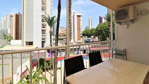A balcony with a table and chairs, overlooking a cityscape with tall buildings and palm trees. - El Junco 4-5 Apartment Levante Beach (Benidorm)