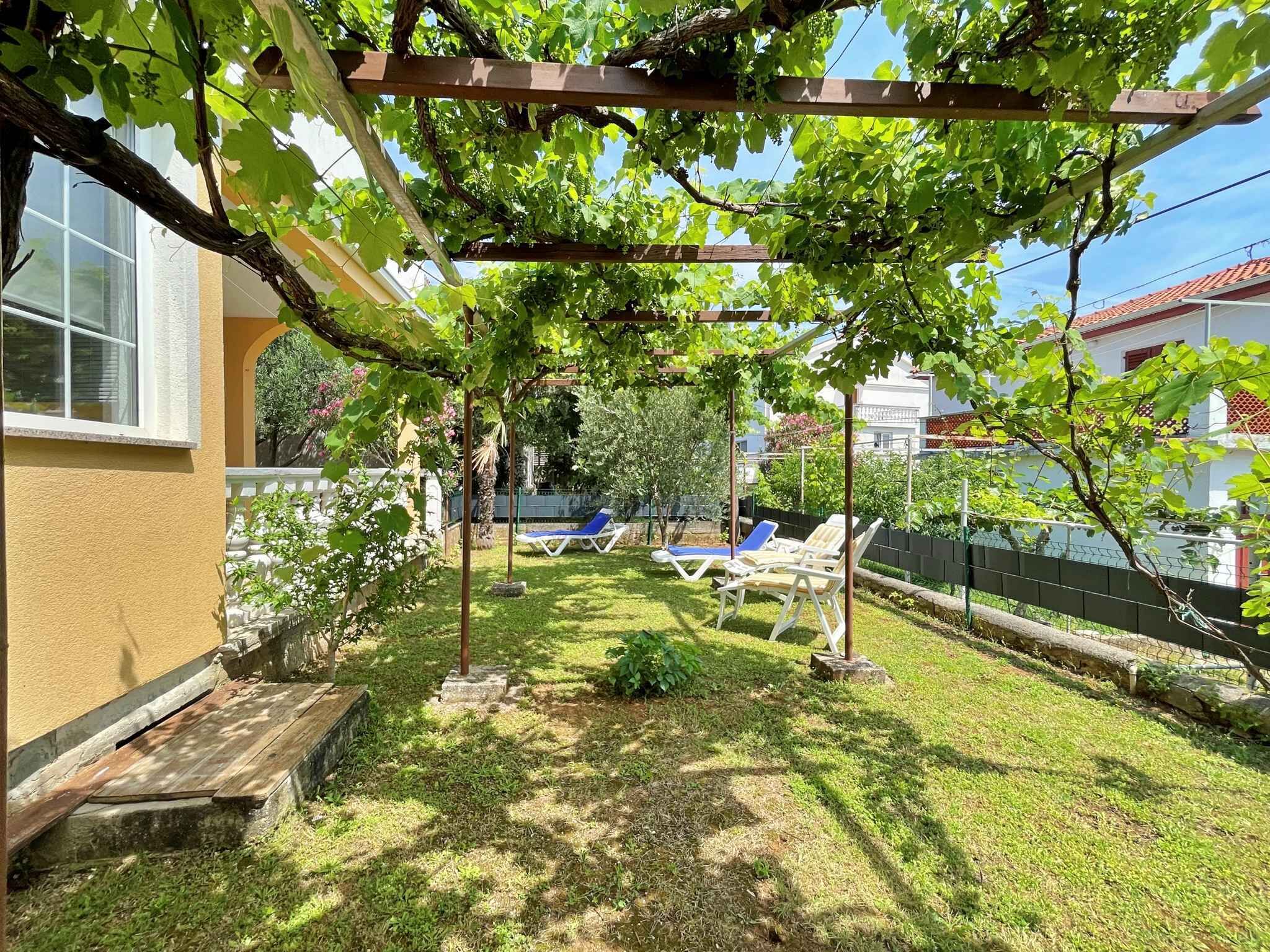 A backyard with a pergola, two lounge chairs, and a small lawn.