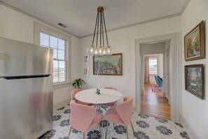 A dining area with a round table, pink chairs, a stainless steel refrigerator, and a chandelier.