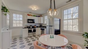A modern kitchen with white cabinets, a central island, and a dining area with a round table and pink chairs. - The Jewel of Bull Street Upstairs - 1 King Bedroom (Columbia)