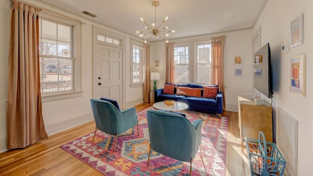 A spacious living room with a blue sofa, two blue armchairs, a coffee table, and a colorful rug. - The Jewel of Bull Street Upstairs - 1 King Bedroom (Columbia)