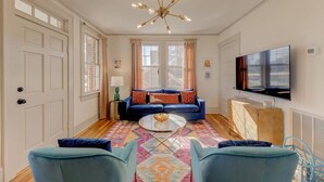 A living room with a blue sofa, a coffee table, and a TV on the wall. - The Jewel of Bull Street Upstairs - 1 King Bedroom (Columbia)