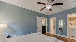 A bedroom with a bed, a ceiling fan, and a door leading to a bathroom.