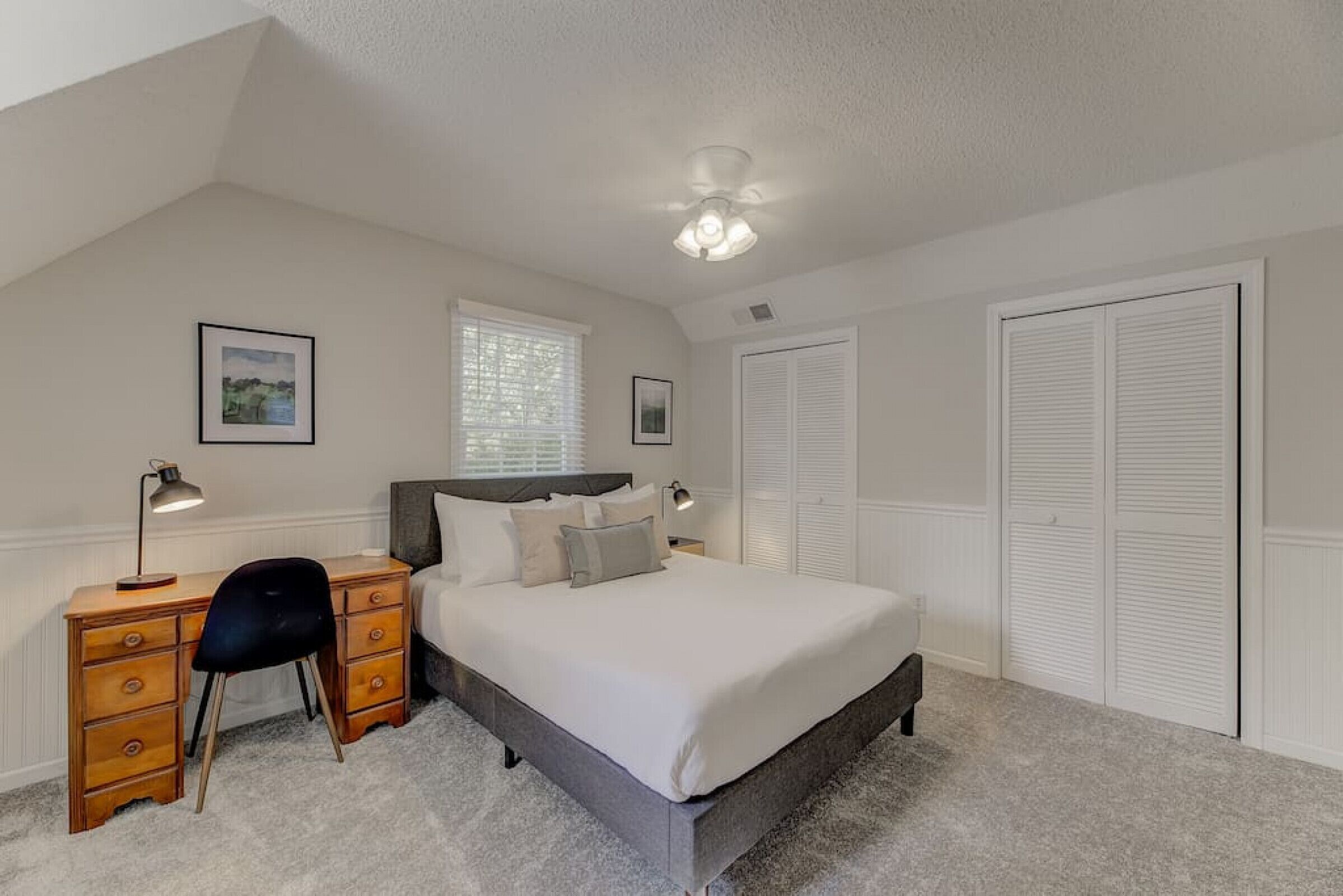 Une chambre à coucher comprenant un lit, un bureau, une chaise, un ventilateur de plafond et une fenêtre avec des stores.