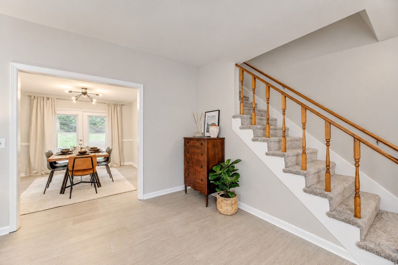 A modern interior with a staircase, a dining area, and a wooden cabinet.
