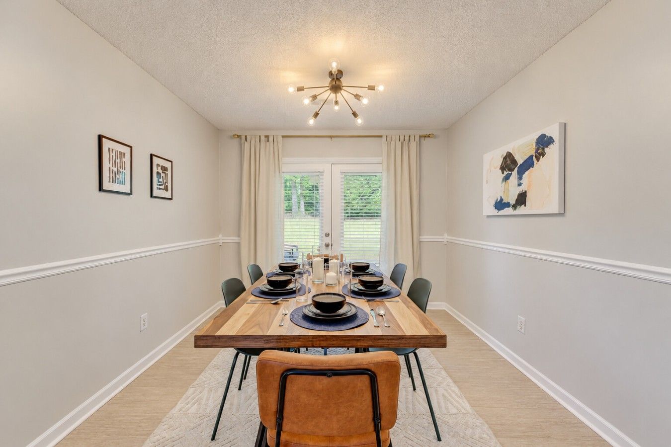 A dining room with a wooden table set for six, flanked by chairs, with a ceiling light fixture above.