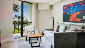 A modern living room with a sofa, a chair, and a table. There is a large window with a view of palm trees.