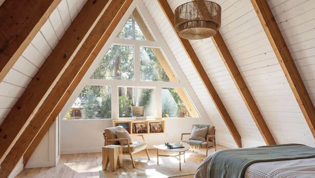 Une chambre confortable située sous les toits, avec un plafond en pente, de grandes fenêtres et un coin salon accueillant.