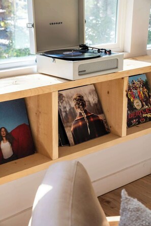 Una habitación con ventana, un tocadiscos blanco Crosley y una estantería con marcos de fotos.