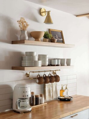 A kitchen with wooden shelves holding various kitchenware, a coffee maker, and hanging mugs.