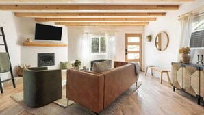 Un salon moderne avec un canapé, un téléviseur fixé au mur, une cheminée et une grande fenêtre avec des rideaux.