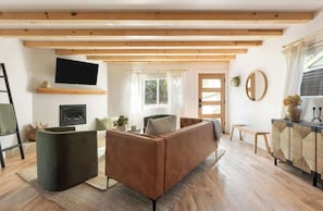 Una sala de estar moderna con un sofá, un televisor instalado en la pared, una chimenea y un ventanal con cortinas.