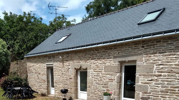 A stone building with a sloped roof, two windows, and a door.