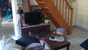 A living room with a wooden staircase, a television on a wooden stand, a sofa, a coffee table, and a wall clock.