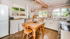 Een keuken met een houten tafel, stoelen, een koelkast, een fornuis en een raam met uitzicht op groen.