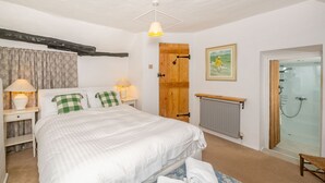Een slaapkamer met een bed, nachtlampjes, een houten deur, een lijst met een afbeelding, een radiator en een douchehoek.