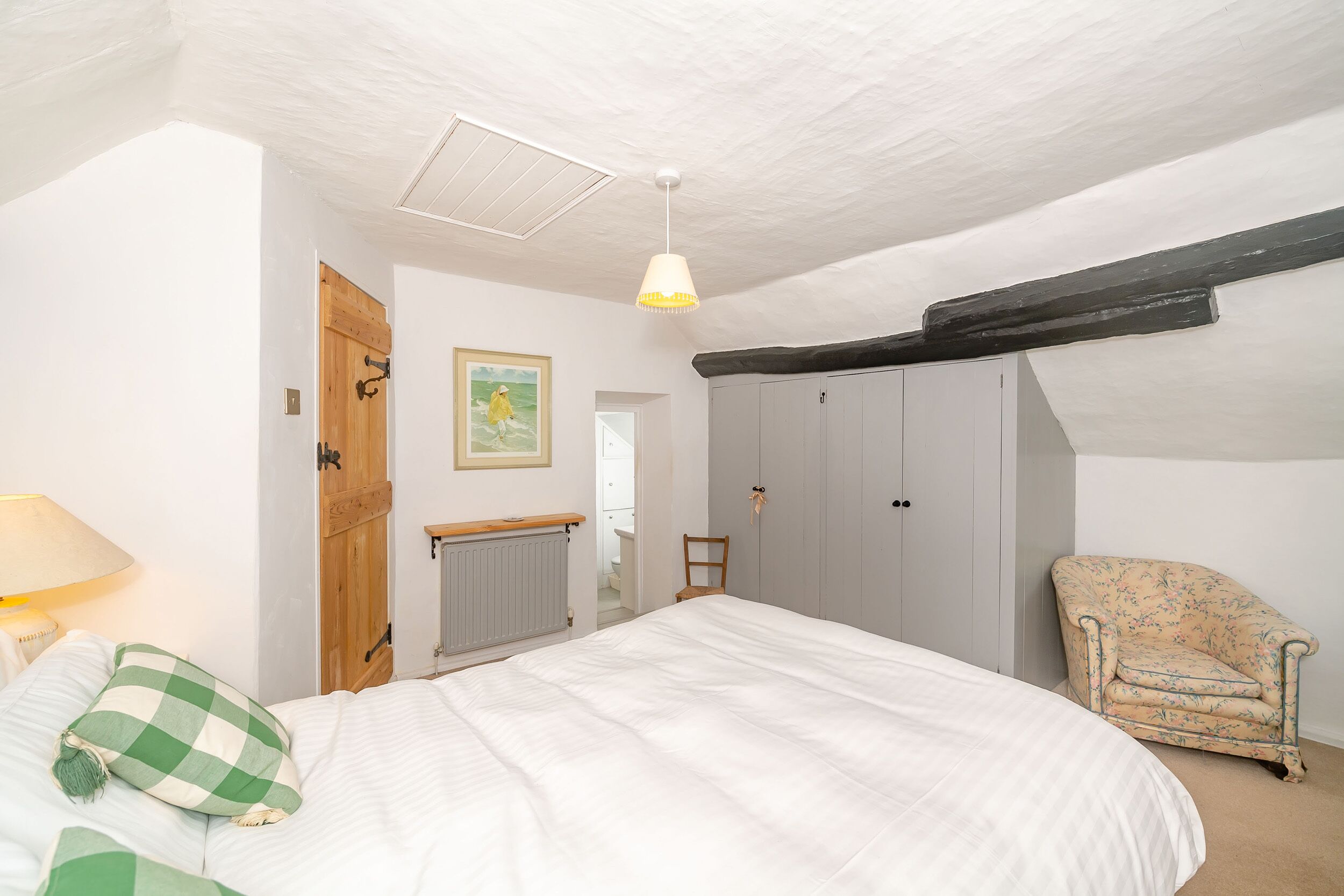 A bedroom with a bed, a chair, a wooden door, and a radiator.