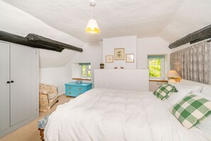 A bedroom with a large bed, a wardrobe, a small table with a lamp, and a chair. - 4 Bishops Cottages (Minehead)