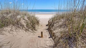 Um caminho de areia serpenteia até o oceano, ladeado por gramíneas altas.