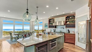 Uma cozinha moderna com uma ilha grande, eletrodomésticos de aço inoxidável e vista para o oceano.